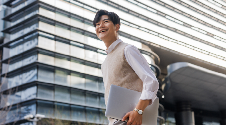 Confident male white-collar adult in smart casual attire walking with laptop in his left hand